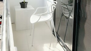 Un balcon avec une chaise blanche, une petite table sur laquelle est posée une plante en pot et une porte vitrée.