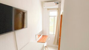 Une petite pièce lumineuse, avec un bureau blanc, une chaise, une plante en pot et une fenêtre avec des rideaux.