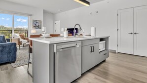 Een moderne keuken met een vaatwasser, een spoelbak en een aanrecht. Er is een eethoek met een tafel en stoelen, en uitzicht op het buitenlandschap door grote ramen.