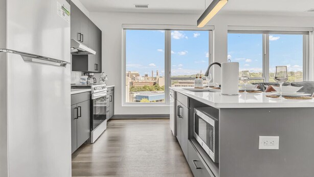 Een moderne keuken met een groot eiland, roestvrijstalen apparatuur en stadszicht door grote ramen.