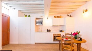 A compact kitchen with white cabinets, a dining table with chairs, and a wooden ceiling.