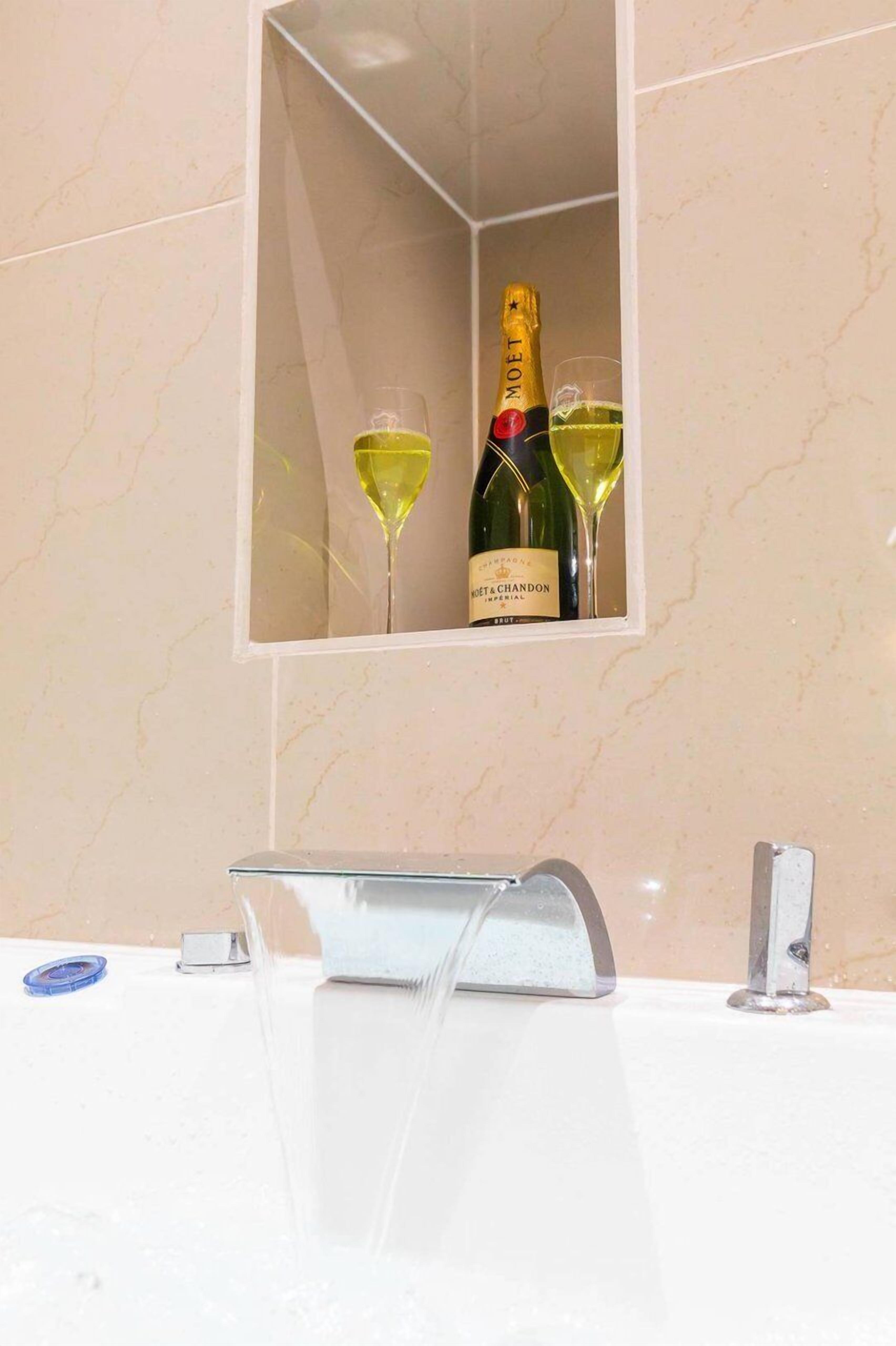 A bathroom with a mirror reflecting a bottle of Moët & Chandon champagne and two glasses.