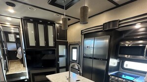 A compact kitchen with a marble countertop, stainless steel appliances, and a bench at the island. - Luxury RV Camper Southern UTAH! (Toquerville)