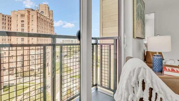 A hotel room with a large window offering a view of a cityscape, a bed, a nightstand, and a lamp. - Peaceful & Relaxing 2BR | Cleveland Clinic (Cleveland)