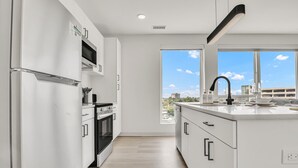 A modern kitchen with white cabinetry, a built-in oven, and a large window offering a city view. - Peaceful & Relaxing 2BR | Cleveland Clinic (Cleveland)