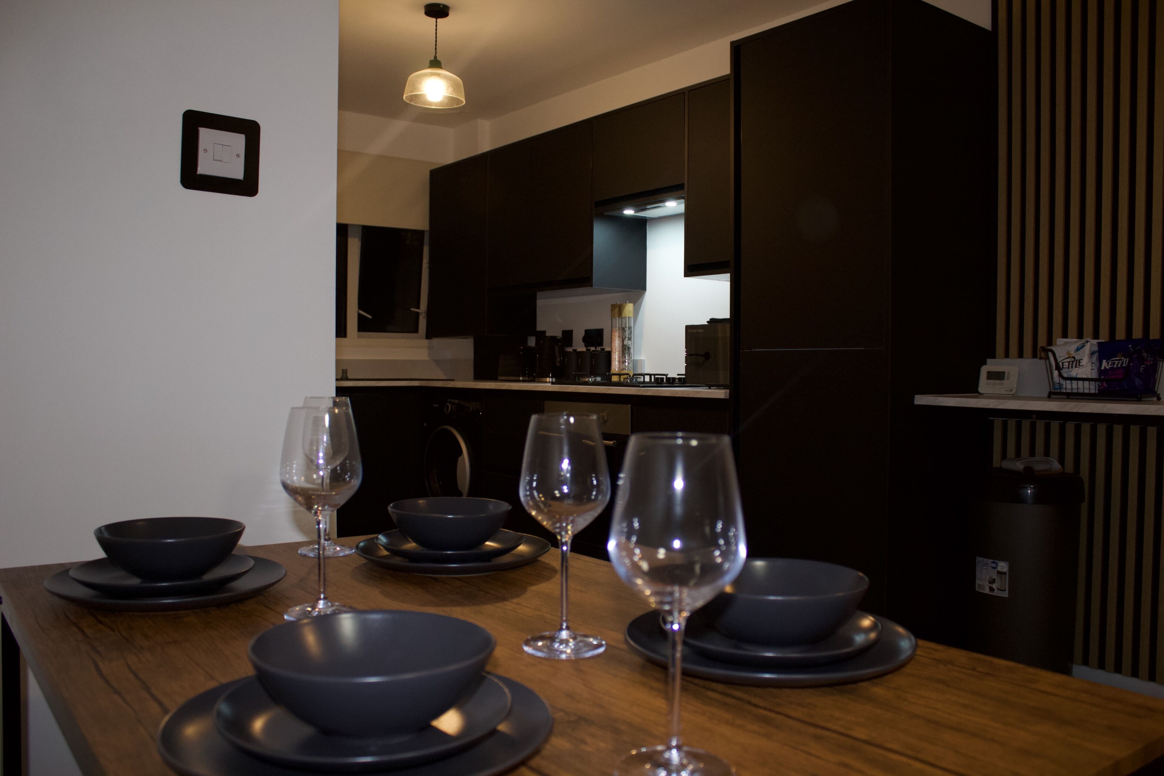A modern kitchen with dark cabinetry, a wooden countertop, and a dining area with a table set for four.
