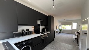 A modern kitchen with black cabinets, a built-in washing machine, and a dining area with a view of the outdoors. - 2 bed House in City Centre - Offers for Long Stays (Nottingham)