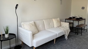 A white sofa with a throw blanket, a small round table with a plant, and a floor lamp. - 2 bed House in City Centre - Offers for Long Stays (Nottingham)