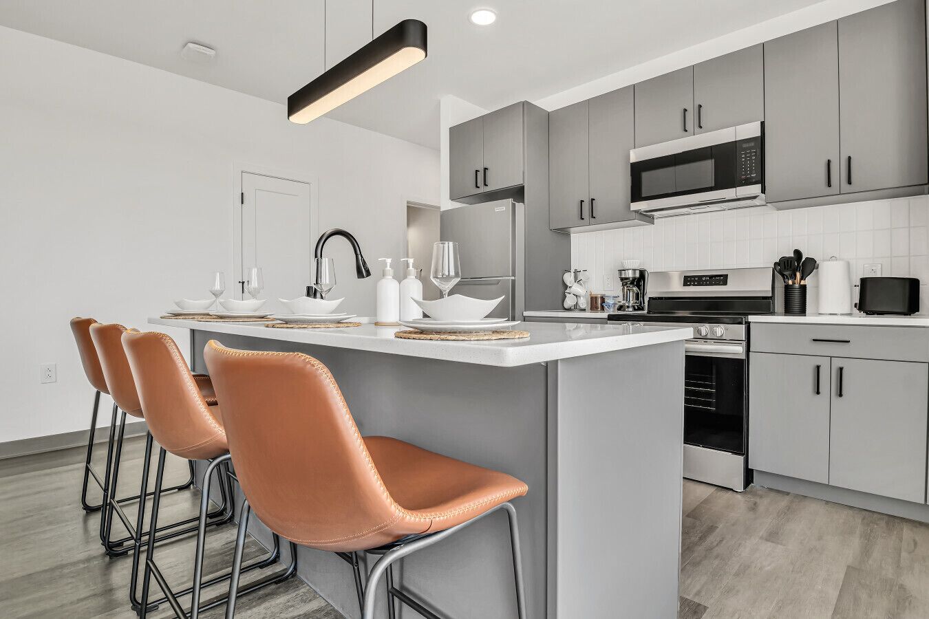 A modern kitchen with grey cabinets, a central island with bar stools, a microwave, and a coffee maker.