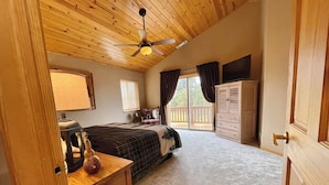 A bedroom with a wooden ceiling, a bed, a dresser, a chair, and a window with curtains.