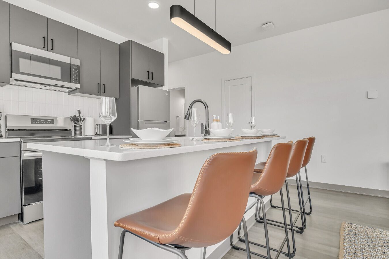 A modern kitchen with white cabinetry, a central island with bar stools, stainless steel appliances, and a pendant light.