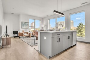 Una cucina moderna con un'ampia isola, zona pranzo con sedie e grandi finestre che offrono vista sulla città.