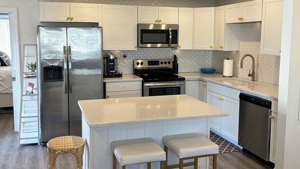 A modern kitchen with white cabinets, stainless steel appliances, and a central island with stools. - Perfect 4-bedroom house in Ocean City, NJ - with Pool (Ocean City)