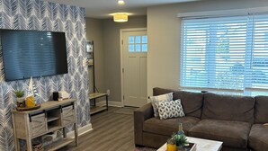 A living room with a large flat-screen TV mounted on a patterned wall, a brown sofa with decorative pillows, a coffee table with a tray of items, and a patterned rug on the floor. - Perfect 4-bedroom house in Ocean City, NJ - with Pool (Ocean City)