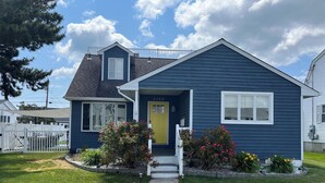 A single-story house with a dark blue exterior, a yellow front door, and a small porch with a white railing. - Perfect 4-bedroom house in Ocean City, NJ - with Pool (Ocean City)
