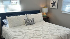 A neatly made bed with a white quilt and two pillows, a blue headboard, a bedside lamp, and a starfish artwork on the wall. - Perfect 4-bedroom house in Ocean City, NJ - with Pool (Ocean City)