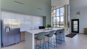 Une cuisine moderne dotée d’un grand îlot central, de tabourets de bar, d’un réfrigérateur en acier inoxydable et d’une fenêtre laissant entrer la lumière naturelle.