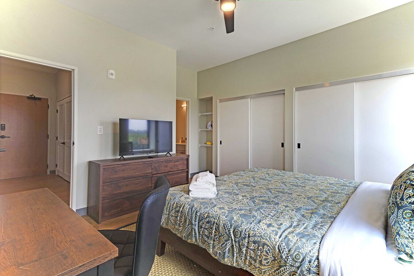 Une chambre d’hôtel avec un lit, un téléviseur posé sur une commode en bois, un bureau et une chaise.