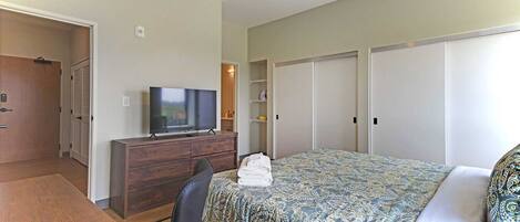 Une chambre d’hôtel avec un lit, un téléviseur posé sur une commode en bois, un bureau et une chaise.