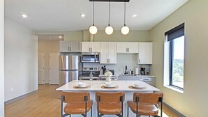 Une cuisine moderne avec des meubles blancs, des appareils en acier inoxydable et un îlot central doté de tabourets de bar.