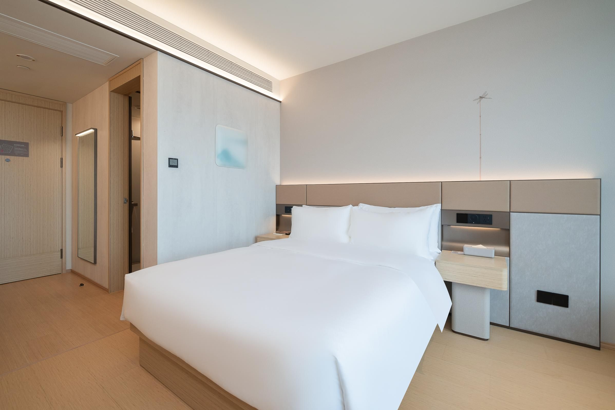 A modern hotel room with a large bed, bedside tables, a wardrobe, and a wall-mounted TV.