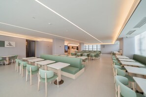 Ett modernt matområde med gröna sittplatser och vita bord, präglat av en stilren, minimalistisk design och gott om naturligt ljus.