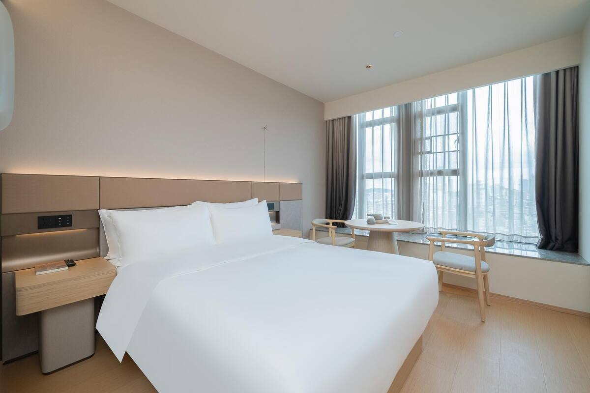 Quarto de hotel com uma cama grande, mesa de cabeceira e uma pequena mesa com cadeiras.