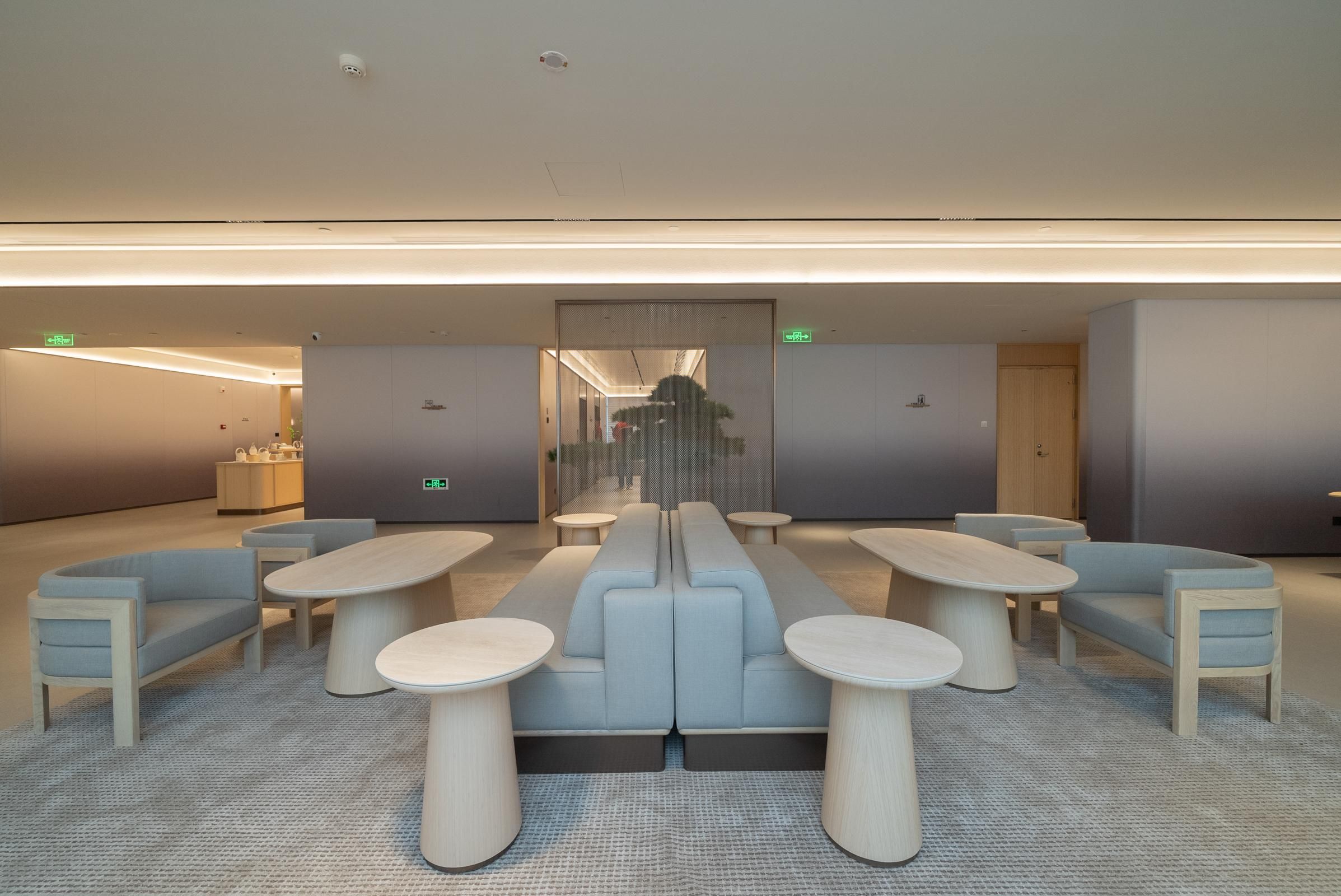 A modern lounge area with seating and tables, a glass partition, and a visible exit sign.