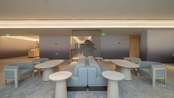 A modern lounge area with seating and tables, a glass partition, and a visible exit sign.