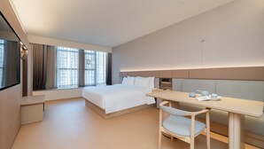 A modern hotel room with a large bed, a desk with a chair, and a window with curtains.