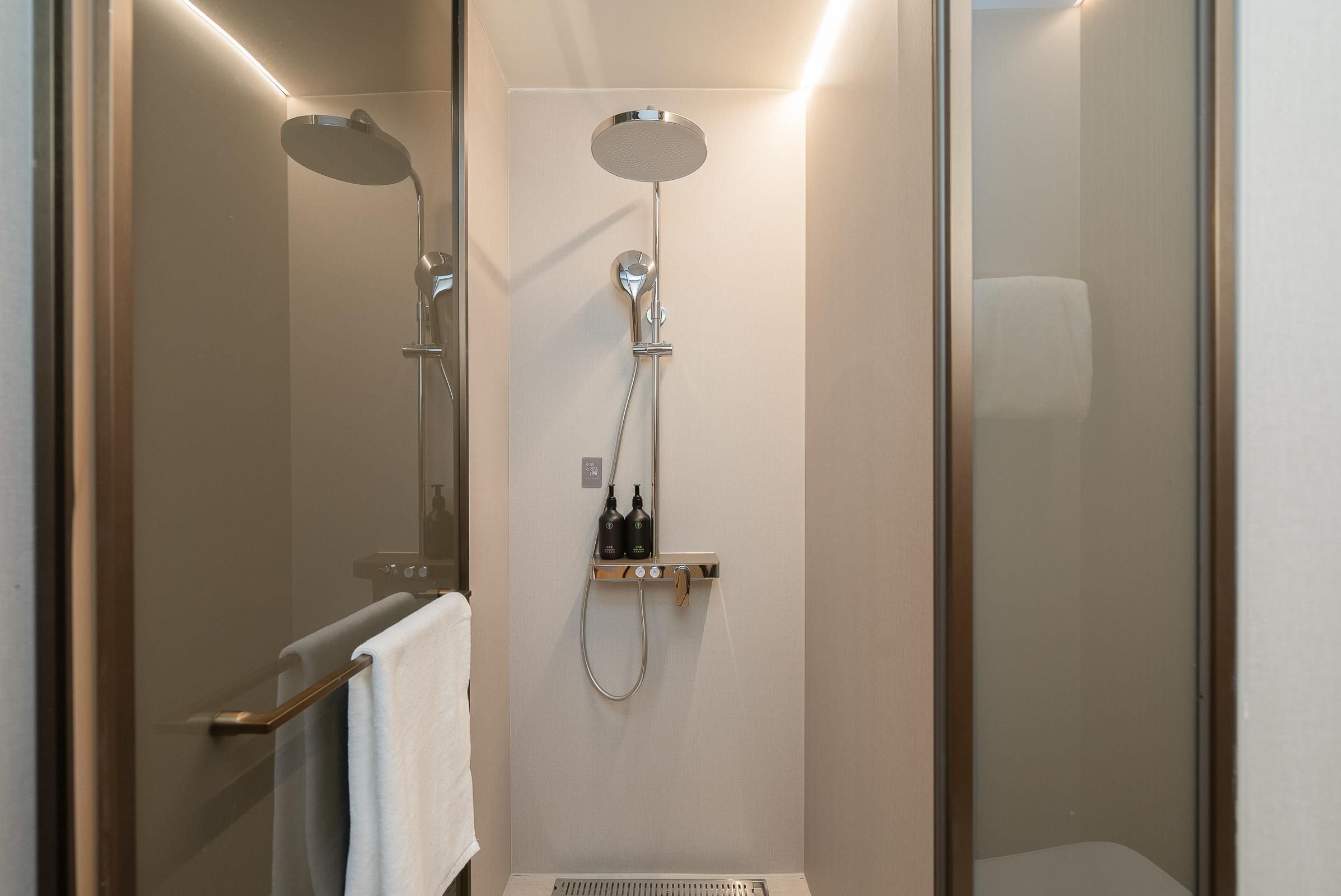 Un área de ducha moderna con puerta de vidrio, ducha de mano y panel de control en la pared.