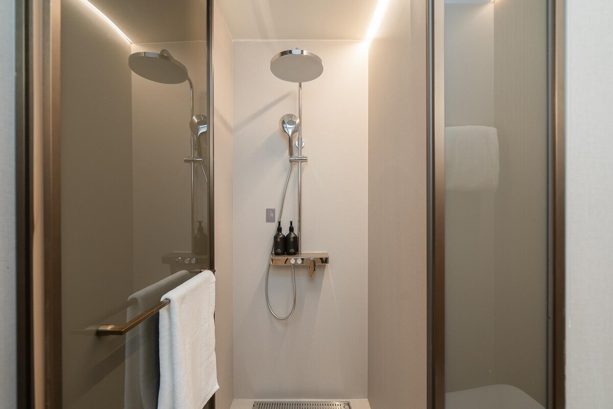 A modern shower area with a glass door, a handheld showerhead, and a wall-mounted control panel.