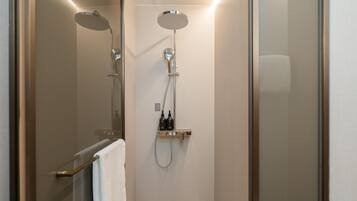 Un área de ducha moderna con puerta de vidrio, ducha de mano y panel de control en la pared.