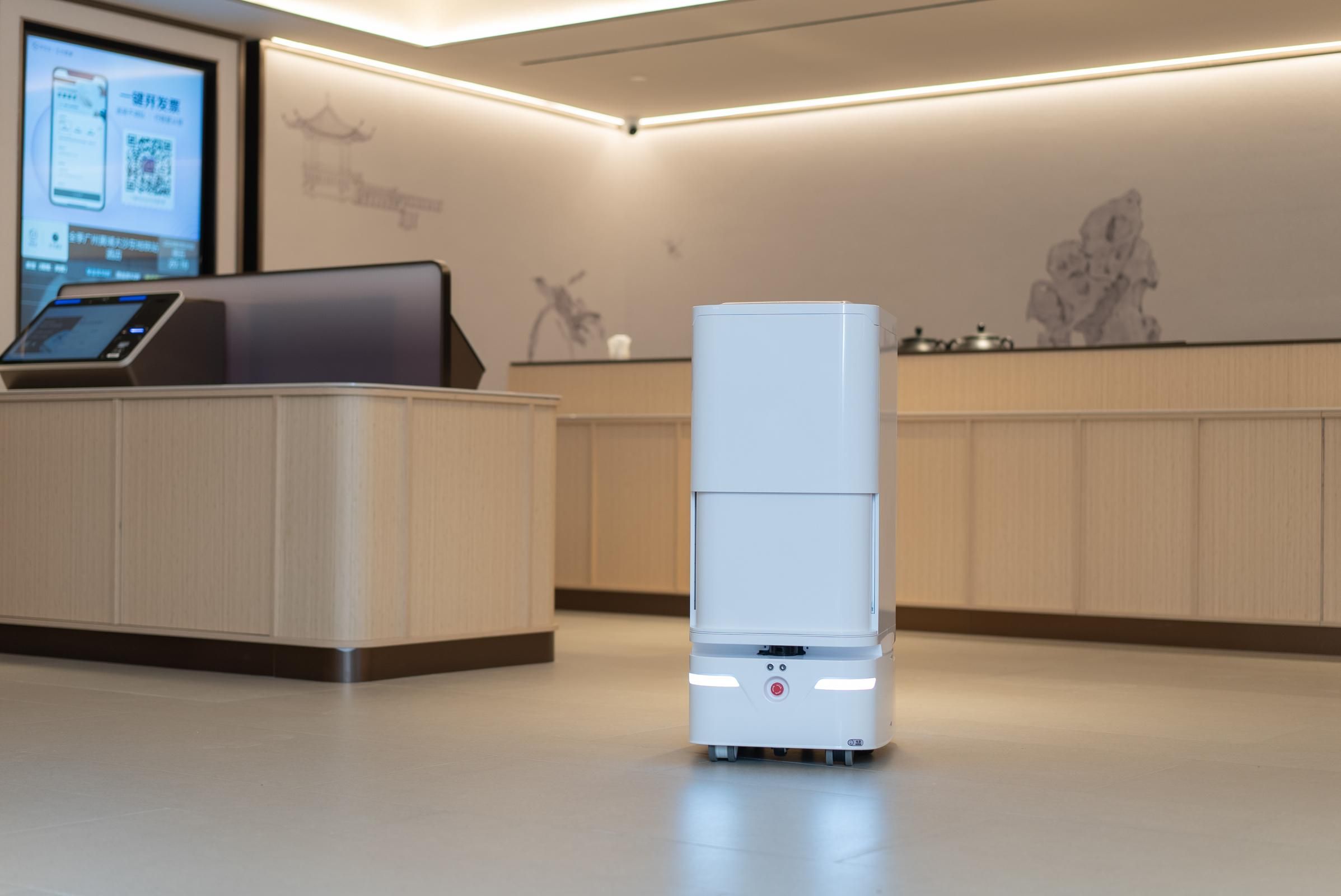 Un vestíbulo de hotel moderno con una recepción, una pantalla digital y un robot.