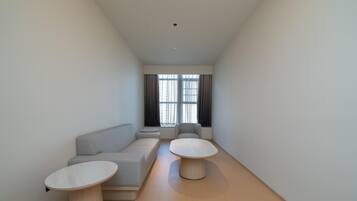 Un salon moderne et minimaliste, avec un canapé, deux tables rondes et une grande fenêtre agrémentée de rideaux.