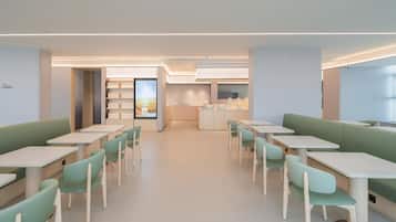 Un comedor moderno con asientos tipo banqueta verdes y mesas blancas, que cuenta con una cocina central y vistas al exterior.