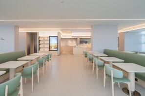 A modern dining area with green booths and white tables, featuring a central kitchen and a view of the outdoors. - Ji Hotel Guangzhou Huangpu East Metro Station (Guangzhou)