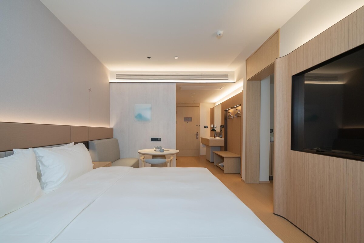 Une chambre d’hôtel moderne avec un grand lit, une petite table ronde, une salle de bain avec un miroir et un téléviseur fixé au mur.