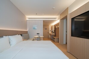 Une chambre d’hôtel moderne avec un grand lit, une petite table ronde, une salle de bain avec un miroir et un téléviseur fixé au mur.