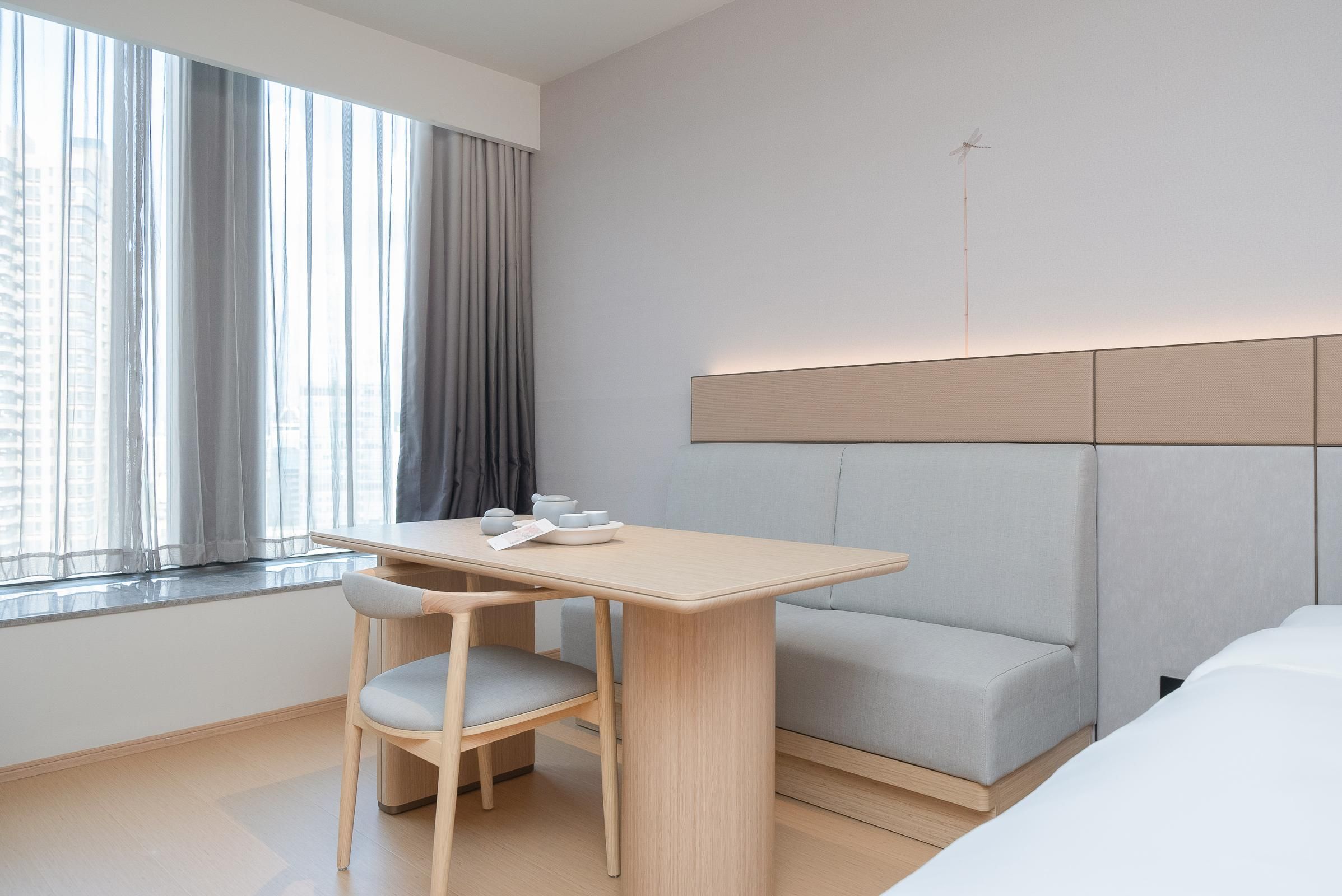 A modern hotel room with a wooden table, a gray sofa, and a window with curtains.
