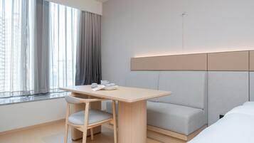 A modern hotel room with a wooden table, a gray sofa, and a window with curtains.