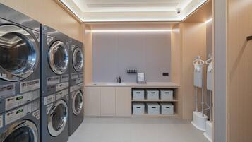 A laundry room with multiple washing machines, a sink, and storage bins.