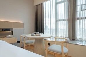 Una camera d'albergo moderna con un tavolo rotondo, due sedie, un letto, un comodino e un'ampia finestra con tende.