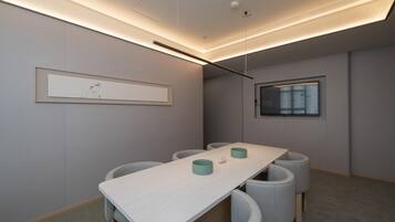 Uma sala de conferências com uma mesa comprida, cadeiras estofadas cinzentas, uma obra de arte emoldurada na parede e uma janela com persianas.