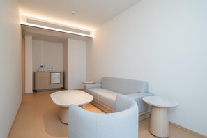 A modern, minimalist living room with a light grey sofa, two round side tables, and a small kitchenette in the background. - Ji Hotel Guangzhou Huangpu East Metro Station (Guangzhou)