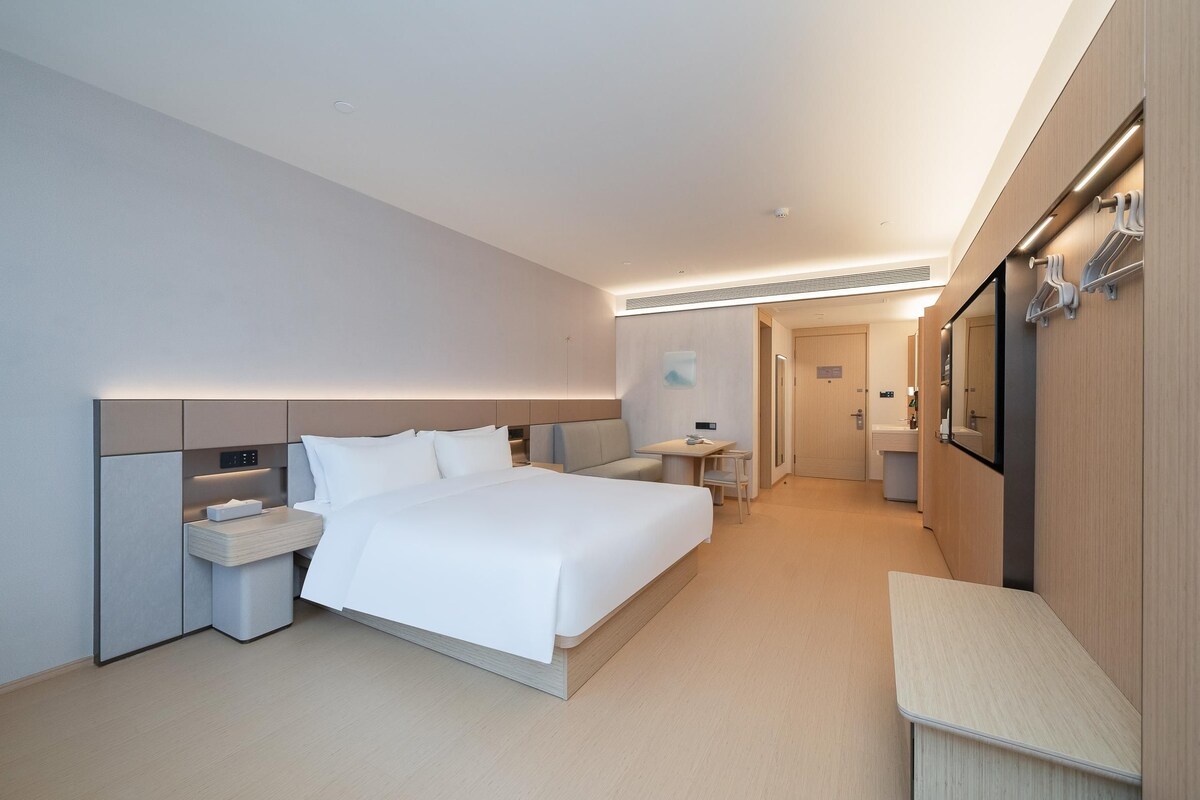 A modern hotel room with a large bed, bedside tables, a small desk, and a bathroom in the background.