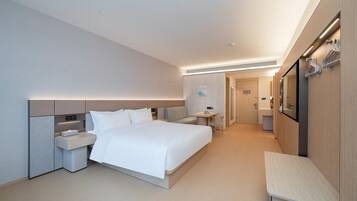 A modern hotel room with a large bed, bedside tables, a small desk, and a bathroom in the background.