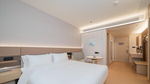 A modern hotel room with a large bed, bedside tables, a small round table, a mirror, and a separate bathroom area. - Ji Hotel Guangzhou Huangpu East Metro Station (Guangzhou)