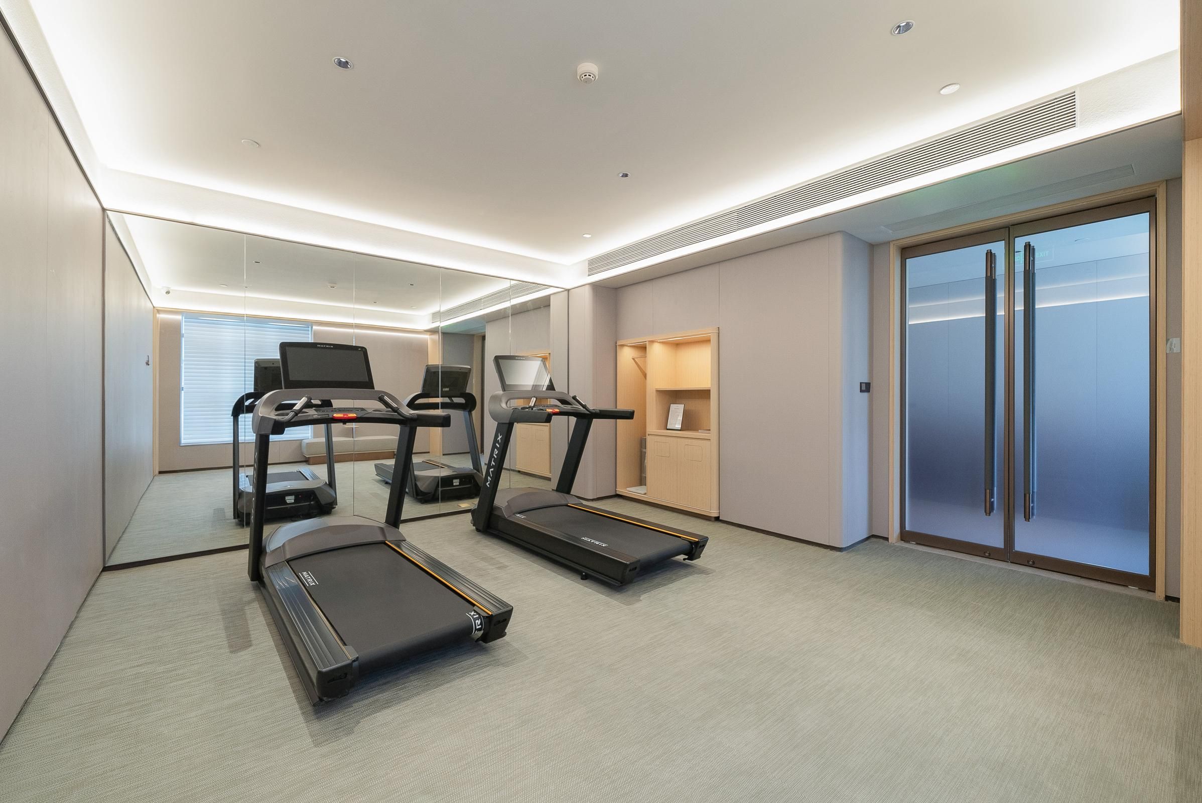 Habitación de hotel moderna con una cinta de correr, bicicleta estática y un espejo grande.