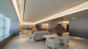 A modern hotel lobby with a sofa, chairs, a kitchen area, and a large window.
